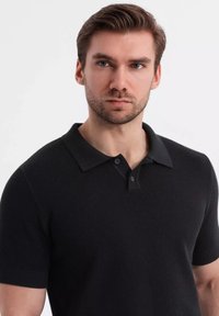 Černé polo tričko s krátkým rukávem vyrobené z texturované tkaniny, se klassickým límcem, zapínáním na dva knoflíky a žebrovanými manžetami na rukávech.