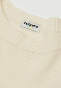 Cremfarbener, gestrickter Pullover für Kinder mit einem gerippten Ausschnitt und einem Etikett mit der Aufschrift "TEZENIS KIDS". Weicher Stoff und leichtes Design.