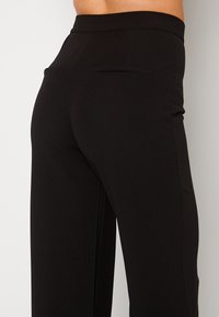 Zwarte broek van glad, stretchy stof, met een aansluitende tailleband, een achterzak en een recht model.