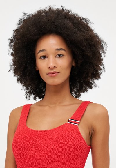 Red textured swimsuit featuring wide straps, a square neckline, and a decorative black and white striped accent on the shoulder strap.