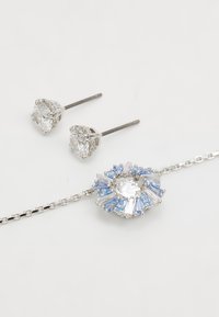 Sølv smykkesæt med et armbånd, der har en cirkulær vedhæng prydet med hvide og blå ædelsten, suppleret af matchende ørestikker.