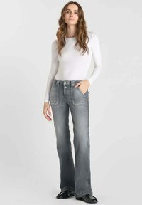 Jeans grises évasés avec poches avant et fermeture à double bouton, associés à un haut ajusté à manches longues blanc. Tissu lisse avec une légère texture.