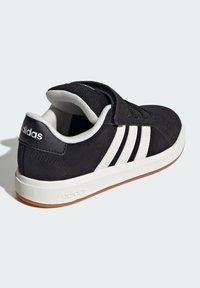 Crni sueden sneakers s bijelim trostrukim uzorkom, gumeni potplat, podstavljena ovratnik i čičak traka za prilagodljivo podešavanje.