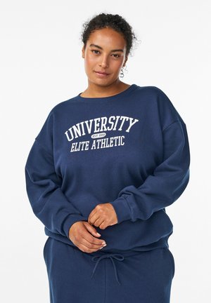 Tumsas, jūras zila kreklis, kas izgatavots no mīksta auduma, ar apaļu kaklu, nolaižamām plecu lineālijām un baltu tekstu "UNIVERSITY ELITE ATHLETIC."