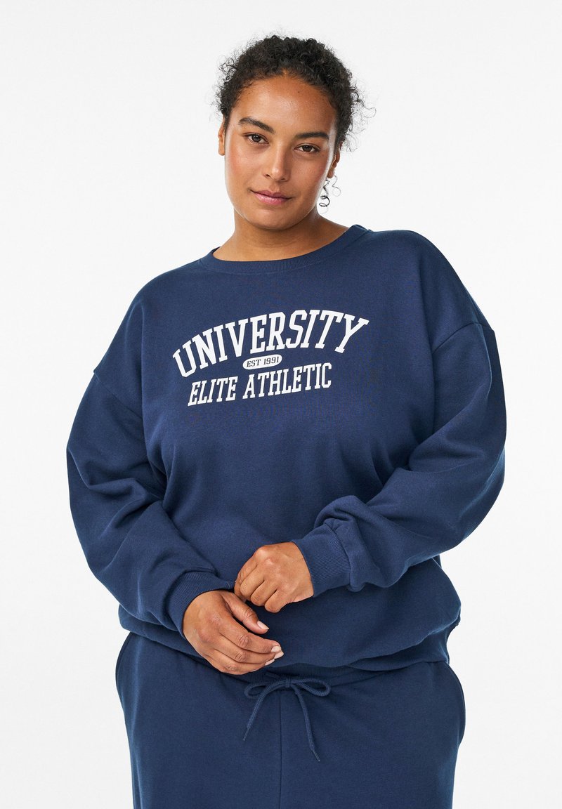 Sudadera azul marino hecha de un tejido suave, con cuello redondo, hombros caídos y texto blanco que dice "UNIVERSITY ELITE ATHLETIC."