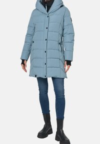 Chaqueta de plumas azul claro con capucha, botones negros, cremalleras laterales y puños acanalados. Lleva puesta con jeans ajustados y botas negras de tobillo.