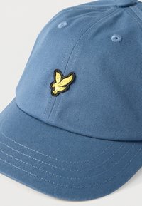 Μπλε μπέιζμπολ καπέλο με κίτρινο έμβλημα πουλιού κεντημένο στο μπροστινό πάνελ και ορατή ραφή στη γείσο.