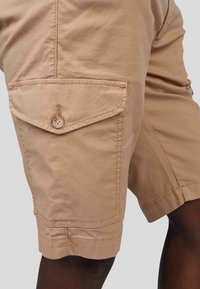 Shorts cargo beige clair en tissu mélangé de coton, dotés d'une poche frontale avec fermeture à bouton et d'empiècements cousus.