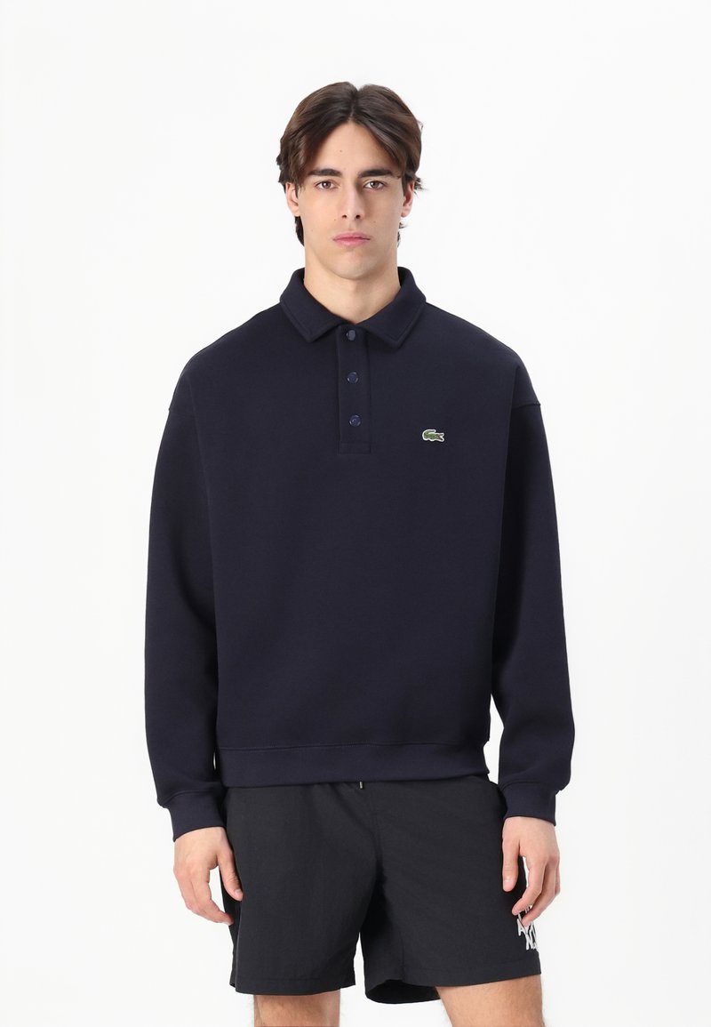Polo de color azul marino con cuello, que presenta tres botones y un pequeño logo verde en el lado izquierdo del pecho. La tela parece suave y ligeramente texturizada.