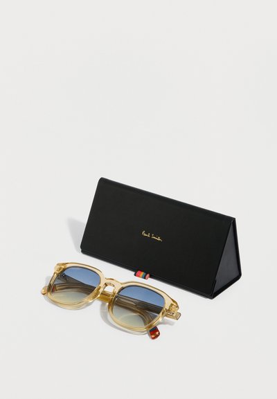 Priehľadné slnečné okuliare z acetátu s modrými šošovkami s prechodom, štvorcovým tvarom a pestrofarebným pruhovaným detailom na bočniciach. Súčasťou je čierne trojuholníkové puzdro.