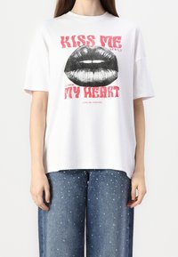 T-shirt bianco a maniche corte con una grande grafica di labbra nere e del testo rosso che recita "BACIOLE GENTILMENTE" e "IL MIO CUORE" in lettere grasse.