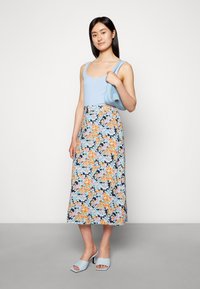 Top sem mangas azul claro, saia midi com padrão floral em flores laranja e azuis, combinada com sapatos de salto bloco azul claro e uma bolsa.