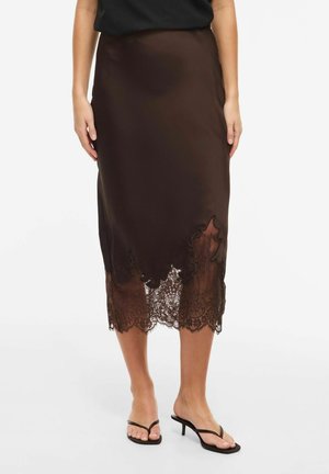 Brun sateng midi skjørt med bølget kant og blonde detaljer, brukt med svarte sandaler med hæl og stropper, og svart topp.