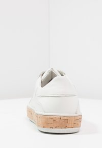 Vita lädersko med en texturerad korksula. Har en rundad form, vadderad ankelsnodd och minimala sömnadsdetaljer.