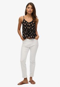 Top de tirantes finos negro con flores, de longitud hasta la cintura, combinado con pantalones ajustados blancos y sandalias marrones de dedo.