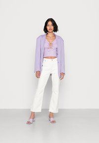 Top cropped lavanda com frente amarrada, combinado com calças brancas de perna larga e sandálias de bloco roxas claras. Texturas suaves em toda a composição.
