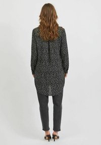 Svart blus med vitt blommönster, långa ärmar, rundad nederkant och knappdetalj på baksidan. Matchad med mörkgrå slim-fit jeans och svarta klackar.