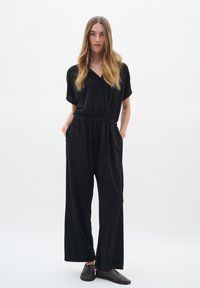 Svart jumpsuit med korta ärmar, V-ringning, elastisk midja och lös, vid byxdress. Stylar med svarta slip-on skor.