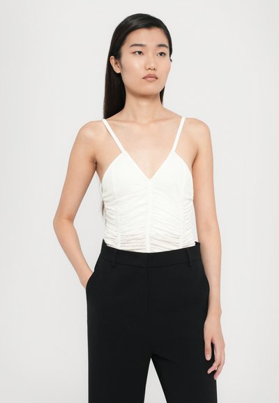 Top blanc ajusté avec un décolleté en V et une texture froncée, associé à un pantalon noir tailleur. Fines bretelles et tissu lisse.