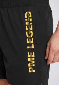 Crne kratke hlače od laganog materijala s bočnom džepom i vertikalnim žutim natpisom "PME LEGEND AMERICAN CLASSIC."