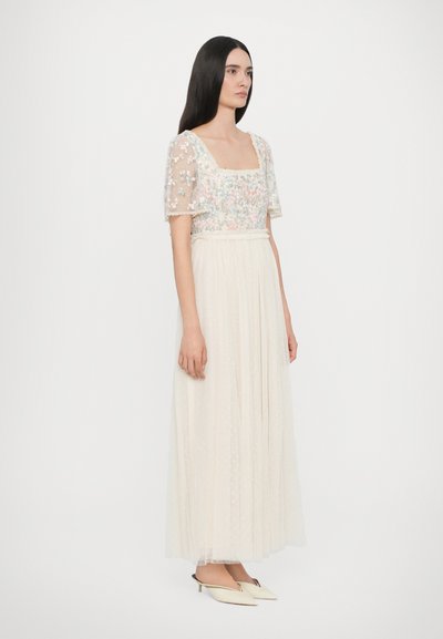 Beige kanten jurk met florale borduursels en korte mouwen, met een vierkante halslijn en een geplooide tule rok. Afgemaakt met crèmekleurige slingback schoenen.
