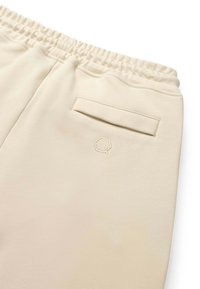 Joggere bej cu talie elastică, buzunar posterior și broderie subtilă cu logo. Material neted cu o textură moale.