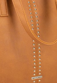 Beige synthetisch leren schoudertas met gouden metalen studdetails in het midden, voorzien van een merketiket aan de onderkant en stevige banden.