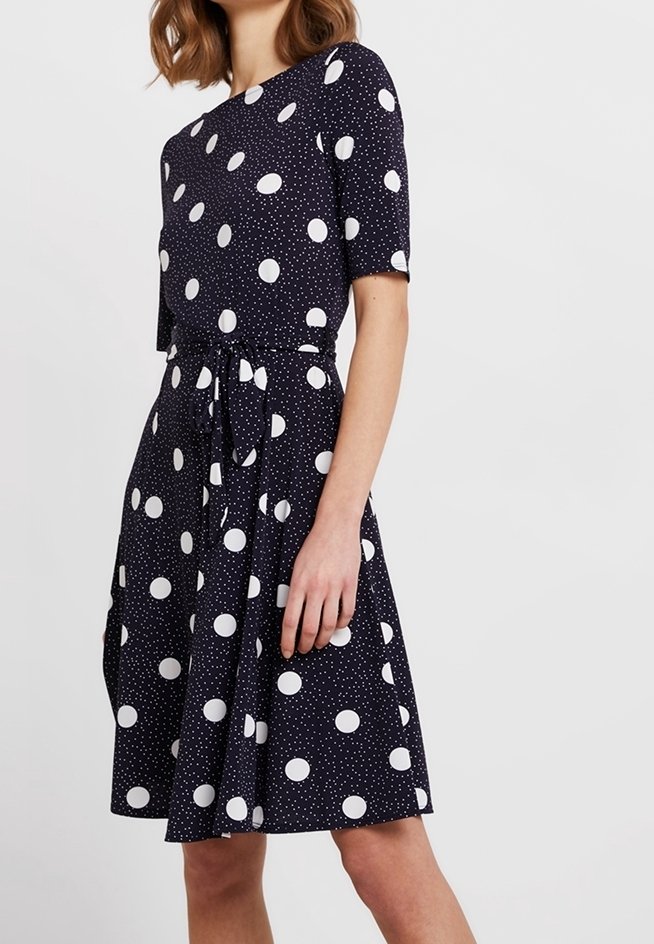 Marinblå klänning med korta ärmar, prydd med vita prickar och små fläckar. Inkluderar ett band i midjan och en utställd kjol. Slät textur.