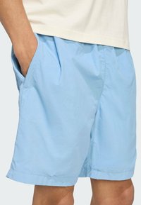 Light blue shorts made of a smooth, lightweight material with side pockets and a relaxed fit. Features an elastic waistband and no visible patterns.