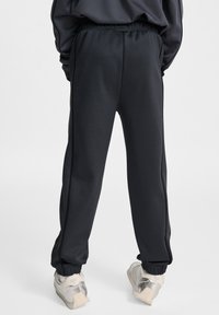 Svarta sweatpants med avslappnad passform, elastisk midja, sidostråk och avsmalnande avslut. Materialet verkar slätt med en lätt lyster.