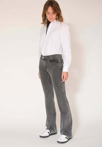 Jeans gris évasés avec une taille mi-haute, un design à cinq poches et un léger effet délavé, associés à une chemise blanche boutonnée et des baskets noires.