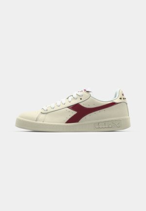 Beige lædersneakers med røde accenter, rund tå og tekstureret gummisål. Har hvide snørebånd og perforerede detaljer på siderne.