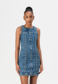 Robe en denim avec un design sans manches, des boutons à l'avant et des détails lacés sur les côtés. Couleur bleu clair avec une texture lisse.