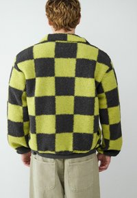 Fleece jack met een dambordpatroon in neon groen en zwart, met een kraag en een ontspannen pasvorm. Zachte textuur, zichtbare naden en zijsplitten.