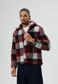 Fleecejack met rood, grijs en wit ruitjespatroon. Voorzien van een kraag, knoopsluiting en een gestructureerde, zachte, pluizige stof.