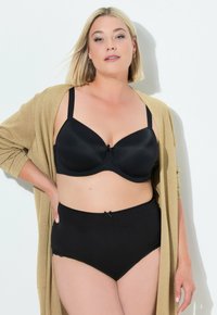 Soutien-gorge noir en tissu lisse, avec soutien-gorge à armatures et nœud décoratif. Culottes noires taille haute assorties avec bords festonnés et détail de nœud. Cardigan doré.