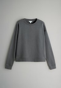 Felpa grigia con maniche lunghe, scollo rotondo e polsini a costine. Texture morbida e vestibilità rilassata senza motivi visibili o accessori.