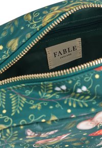 Green fabric pouch with a gold zipper; features a whimsical floral and fauna pattern; tag reads "FABLE ENGLAND."