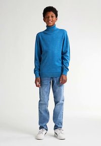 Niebieski sweter z golfem z miękkiej dzianiny, z długimi rękawami; zestawiony z jasnoniebieskimi dżinsami i białymi trampkami.