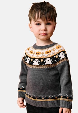 Jeune garçon aux cheveux courts et bruns portant un pull gris avec des motifs orange et blancs sur le thème d'Halloween, incluant des fantômes et des citrouilles.