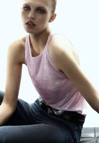 Top sin mangas de color rosa brillante con un escote redondeado, combinado con jeans de mezclilla azul oscuro y un cinturón negro con una hebilla plateada.