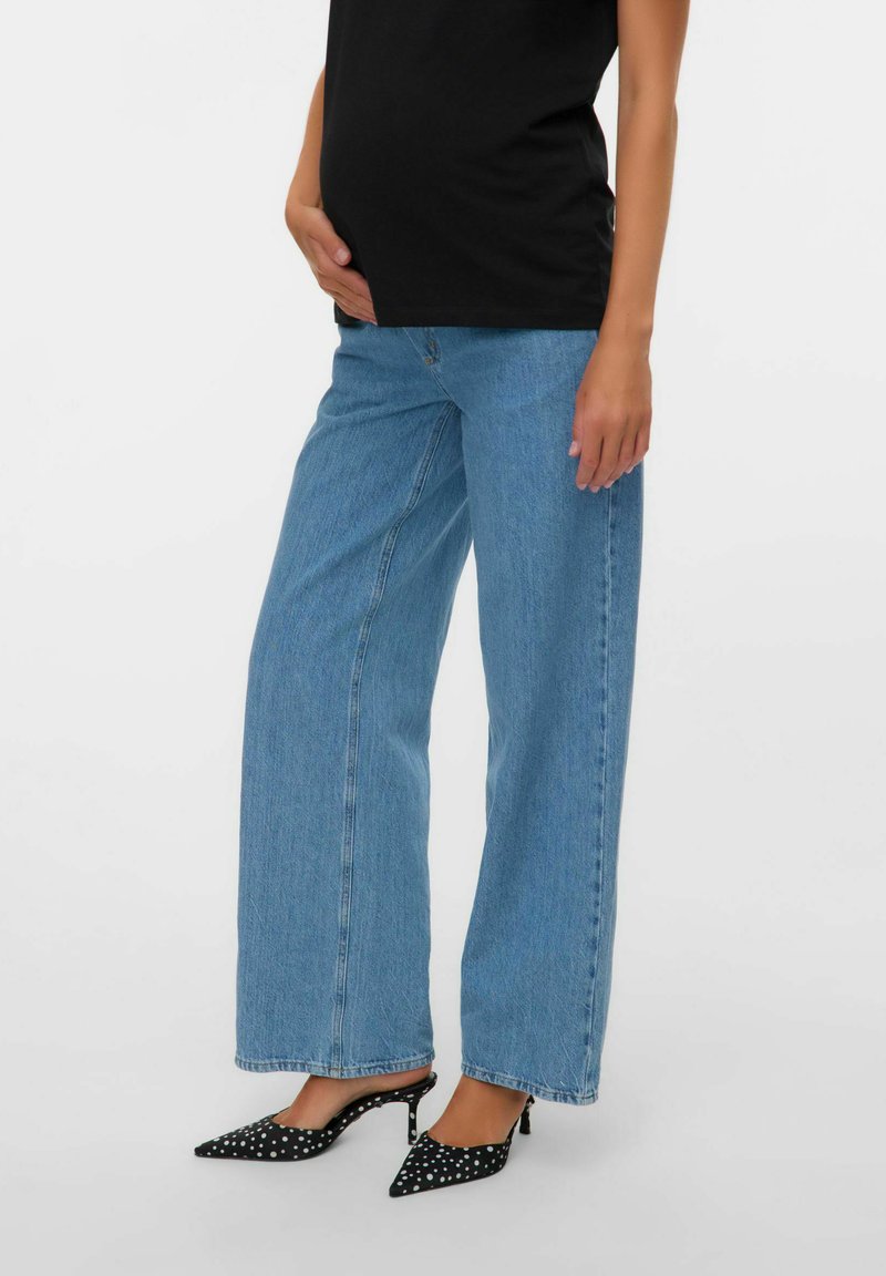 Jeans de pierna ancha de color azul claro con cintura alta, hechos de denim, combinados con tacones de slingback negros con lunares blancos.