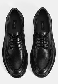 Schwarze Lederschuhe mit strukturiertem Finish, runder Spitze, Schnürdesign und Gummisohlen mit geripptem Rand. Innen mit "DESA" markiert.