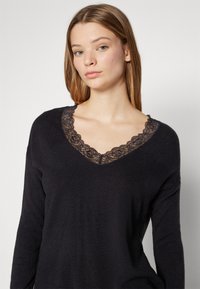 Zwart gebreid sweater met lange mouwen en een V-hals ontwerp met kantafwerking. Zachte textuur, met complexe bloemenkant accenten bij de halslijn.