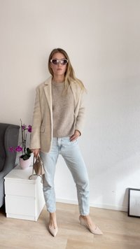 Beige gyapjú keverék blézer egy világosbarna kötött pulóver felett, világos farmernadrággal és meztelen, hegyes orrú magassarkú cipővel párosítva. Kiegészítők között napszemüveg és egy kis kézitáska található.