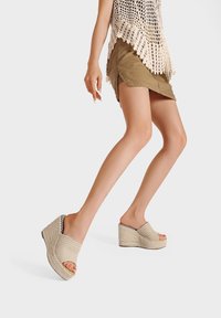 Sandali con zeppa beige, con tomaia in tessuto intrecciato, design open-toe e suola testurizzata. Presentano un accento interno a strisce bianche e nere.