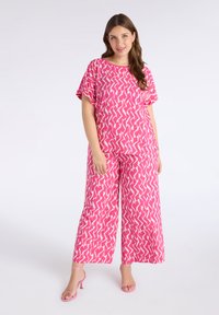 Top de color rosa con estampado y pantalones de pierna ancha con un diseño en zigzag en crema, hechos de una tela ligera. Completado con tacones rosas con tiras.