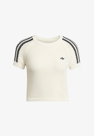 Kremowy prążkowany crop top z teksturowanej dzianiny, krótkie rękawy i czarne paski na ramionach. Z małym czarnym logo.