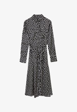 Schwarzes Kleid mit weißen Punkten, langen Ärmeln, Kragen, Knopfleiste, zwei Brusttaschen und einer Taillenschnürung.