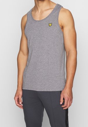 Mand iført en grå ærmeløs tanktop med en lille gul fuglelogo på venstre bryst, kombineret med mørkegrå bukser.